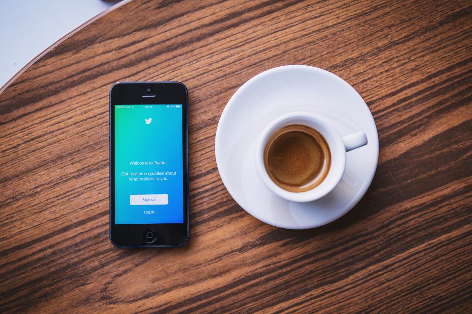 cup of coffee next to phone showing twitter login as example of what is social relationship management all about